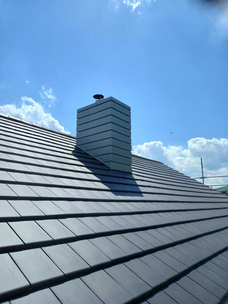 Moderner Schornstein mit Metallverkleidung auf frisch gedecktem Ziegeldach unter blauem Himmel.