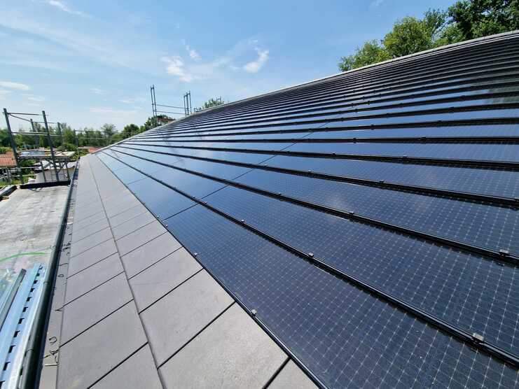 Fachgerechte Montage von Solarmodulen auf einem geneigten Dach durch eine professionelle Bauklempnerei bei sonnigem Wetter.