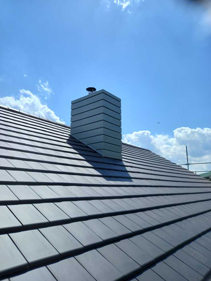 Moderner Schornstein mit Metallverkleidung auf frisch gedecktem Ziegeldach unter blauem Himmel.