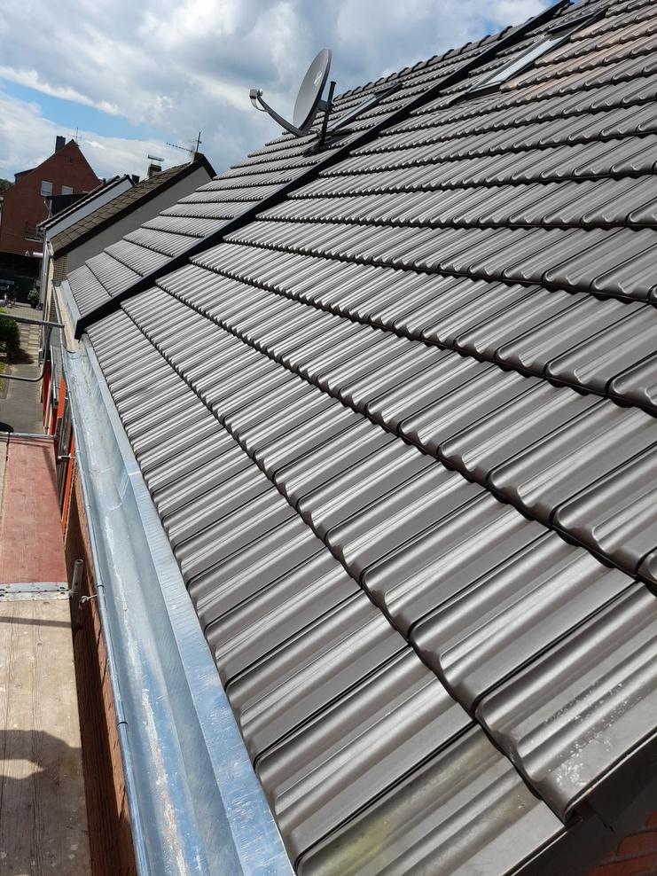 Schr&auml;gdach mit neuen dunkelgrauen Dachziegeln, Sat-Sch&uuml;ssel und sauberer Regenrinne.