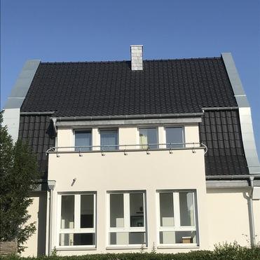 Sanierung Wohnhausdach mit Ziegeln Zweigeschossiges Wohnhaus mit saniertem schwarzem Ziegeldach und heller verputzter Fassade.
