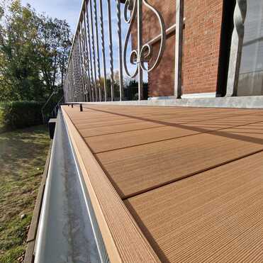 Balkon mit neuem Holzoptik-Belag und verziertem Metallgel&auml;nder, montiert durch Dachdeckerbetrieb.