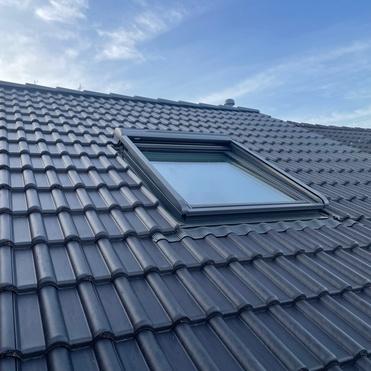 Dunkles Ziegeldach mit neu eingebautem Dachfenster und sauber eingepasster Abdichtung.