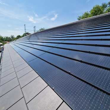 Fachgerechte Montage von Solarmodulen auf einem geneigten Dach durch eine professionelle Bauklempnerei bei sonnigem Wetter.