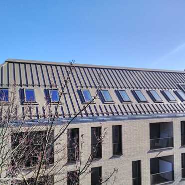 Mehrfamilienhaus mit steilem Metalldach und zahlreichen eingebauten Dachfenstern.