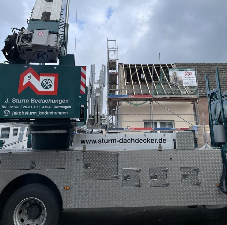 Ein großer, mobil montierter Kran an einer Baustelle, der vor einem Haus mit Gerüst steht. Der Himmel ist bewölkt.